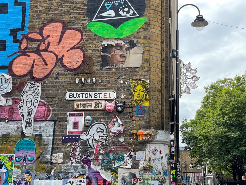 Cartello Buxton St circondato dalla street art nel quartiere di Brick Lane, con scritta in inglese e hindi