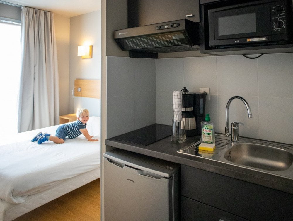 Vista di un monolocale dell'Aparthotel Adagio Dijon République a Digione, con cucina e bambino sul letto